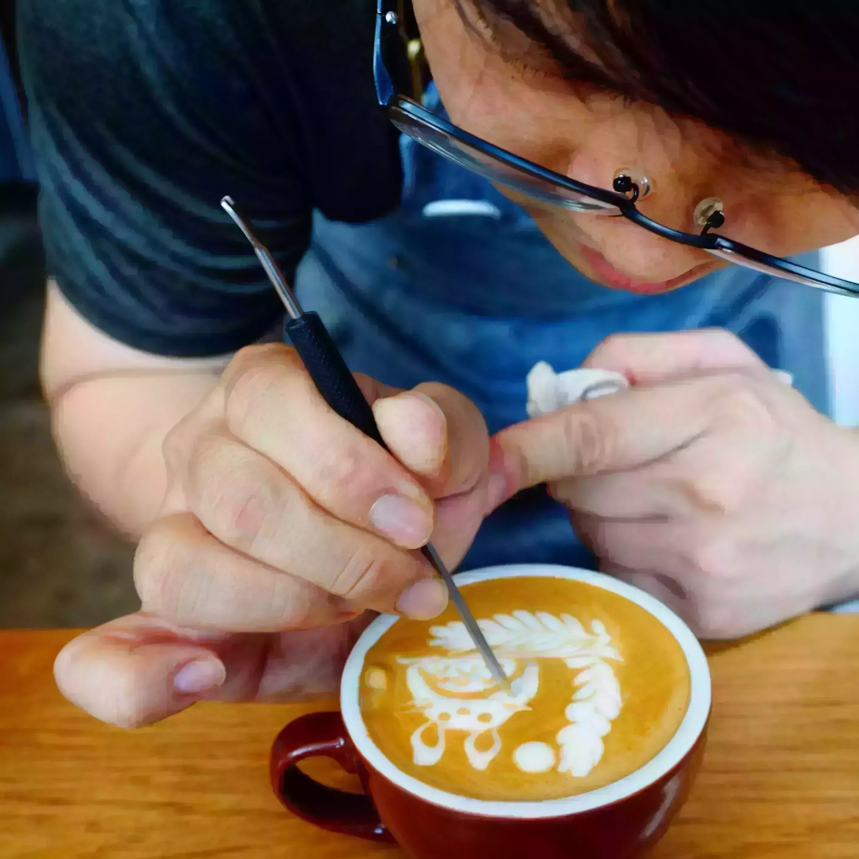 midsection of man making froth art in coffee cup on table