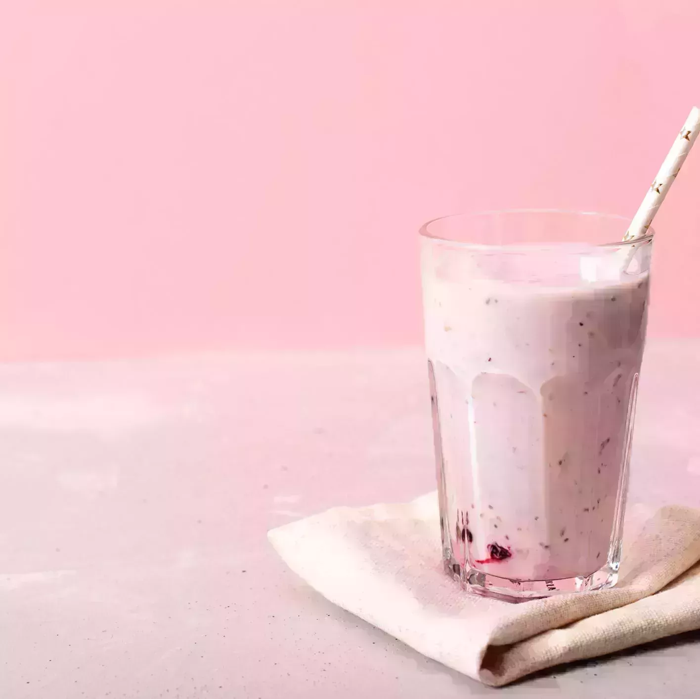 two glasses of blueberries smoothie on pink background poring from blender into glass