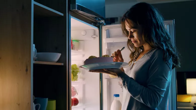 Mujer comiendo frente al refrigerador